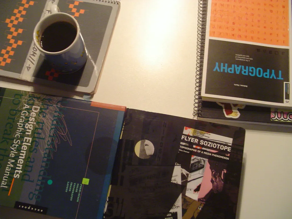 Design books, a spiral notebook and a mug of coffee laid out on a desk