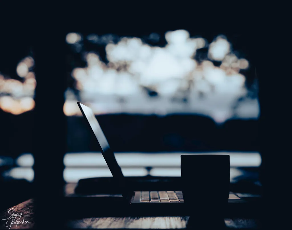 A laptop and a mug silhouetted against a bright window