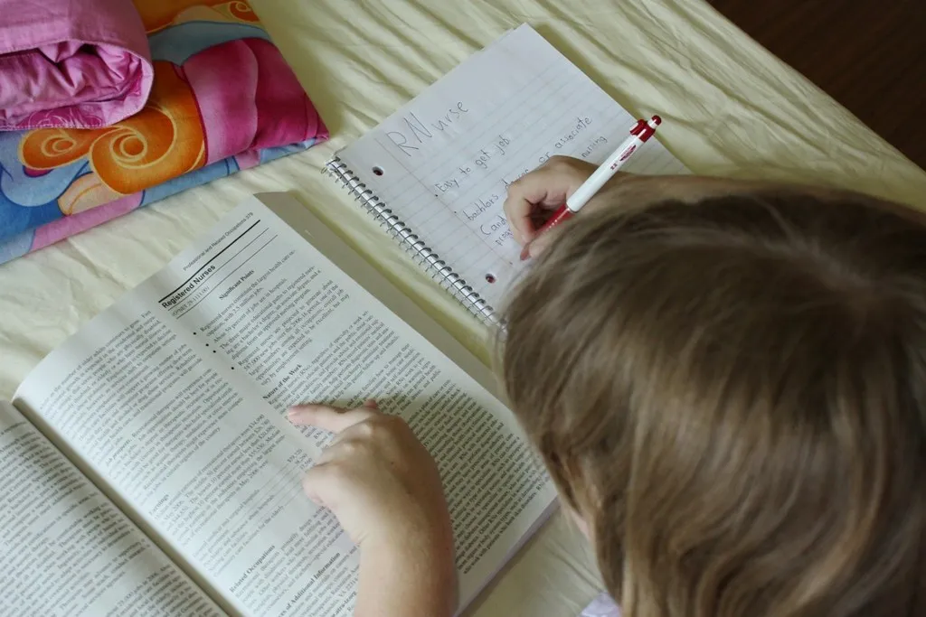 A student taking handwritten notes from an open textbook
