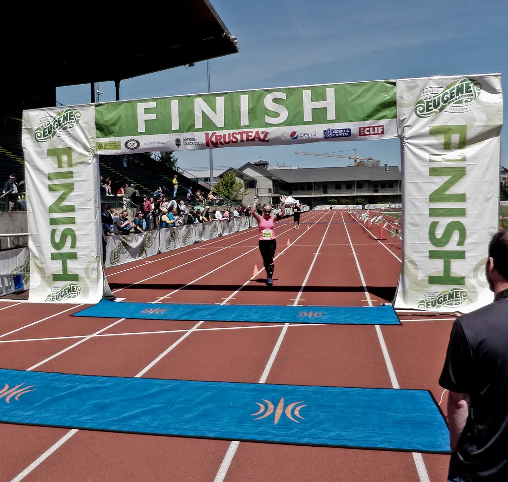 A runner crossing the finish line arch of a marathon with arms raised