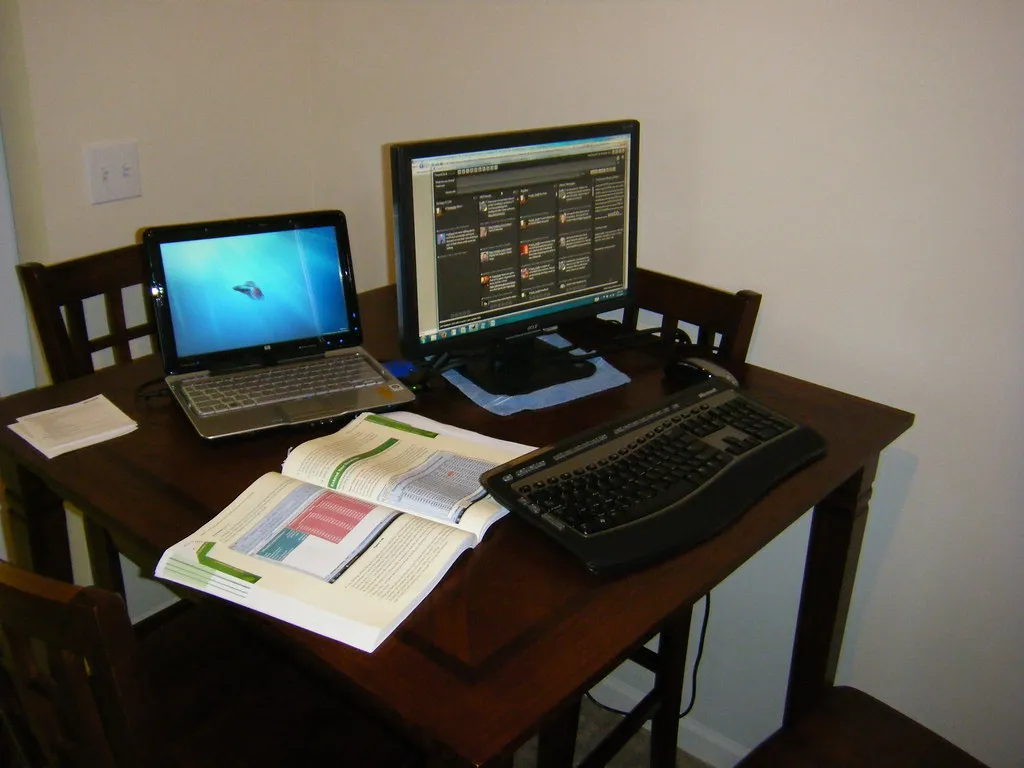 An office desk with a laptop, an external monitor and an open textbook