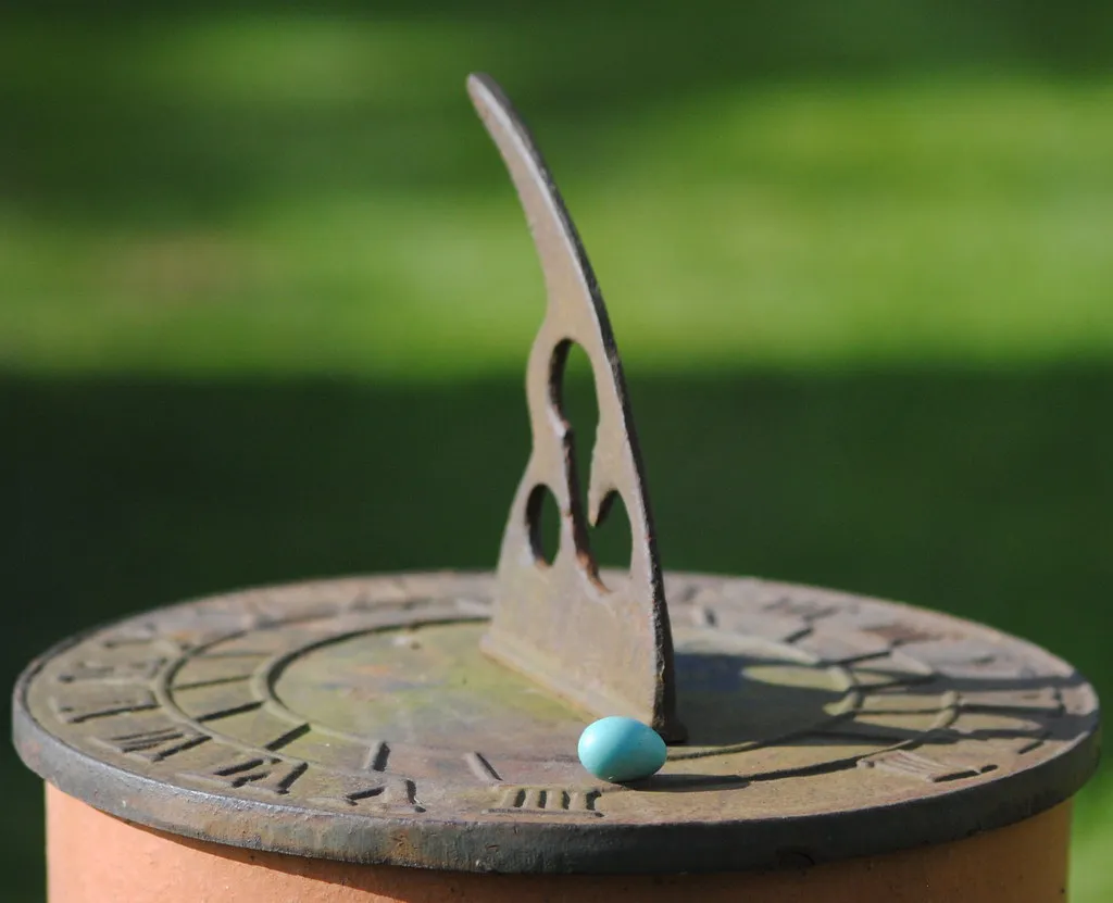 A small blue egg resting on the face of a garden sundial