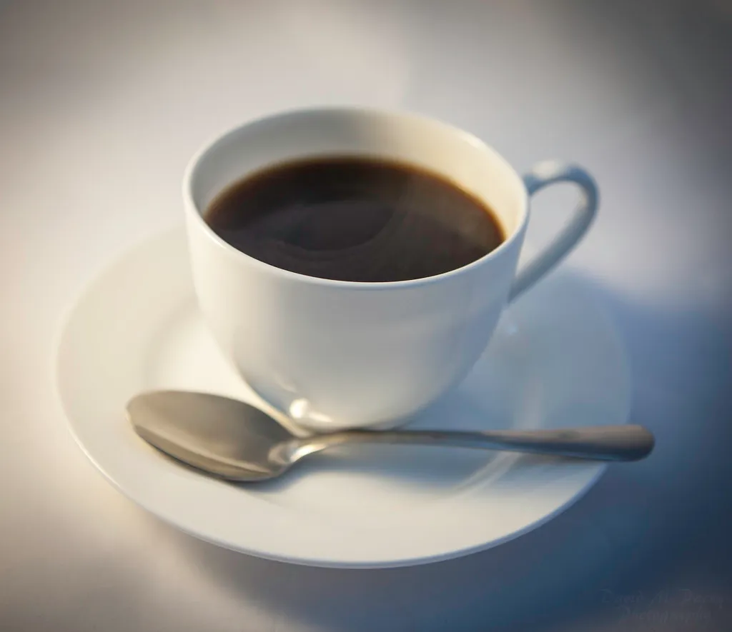 A cup of black coffee on a saucer with a spoon