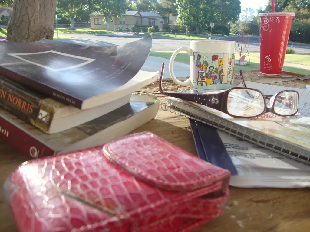 A stack of books, a mug and reading glasses on an outdoor table
