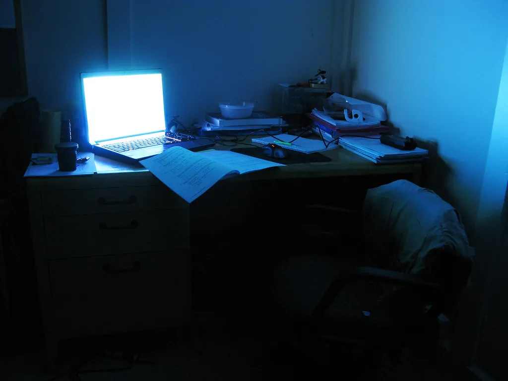 A glowing laptop on a desk covered in notes late at night