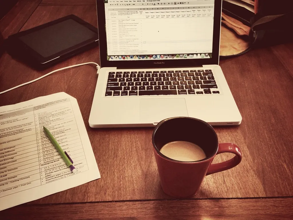 A home desk with a laptop, paperwork and a red mug of coffee